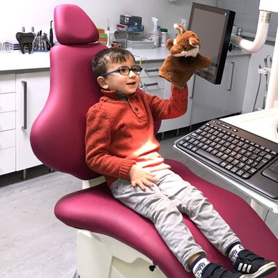 Un enfant souriant avec un gant en peluche lors d'une consultation dentaire pour enfants, dans un cabinet d'orthodontie moderne.